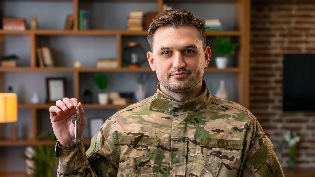 Indoor shot of military man wearing camouflage uniform and hat holding house keys, mortgage assistance from a veterans organization, extremely happy soldier male